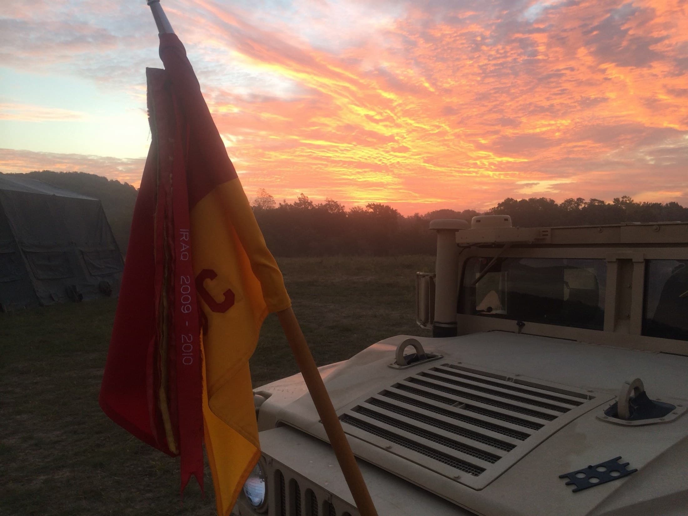 A cavalry troop guidon embroidered IRAQ 2009–2010 mounted on a Humvee at sunset in the field