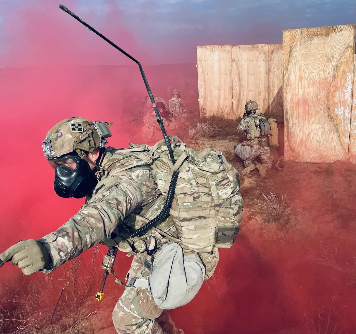 Active duty soldiers in full kit moving through red smoke during training