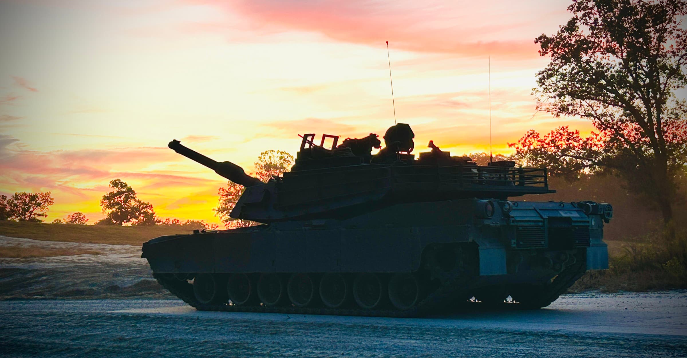 An M1 Abrams main battle tank silhouetted against a burning sunset on a training range