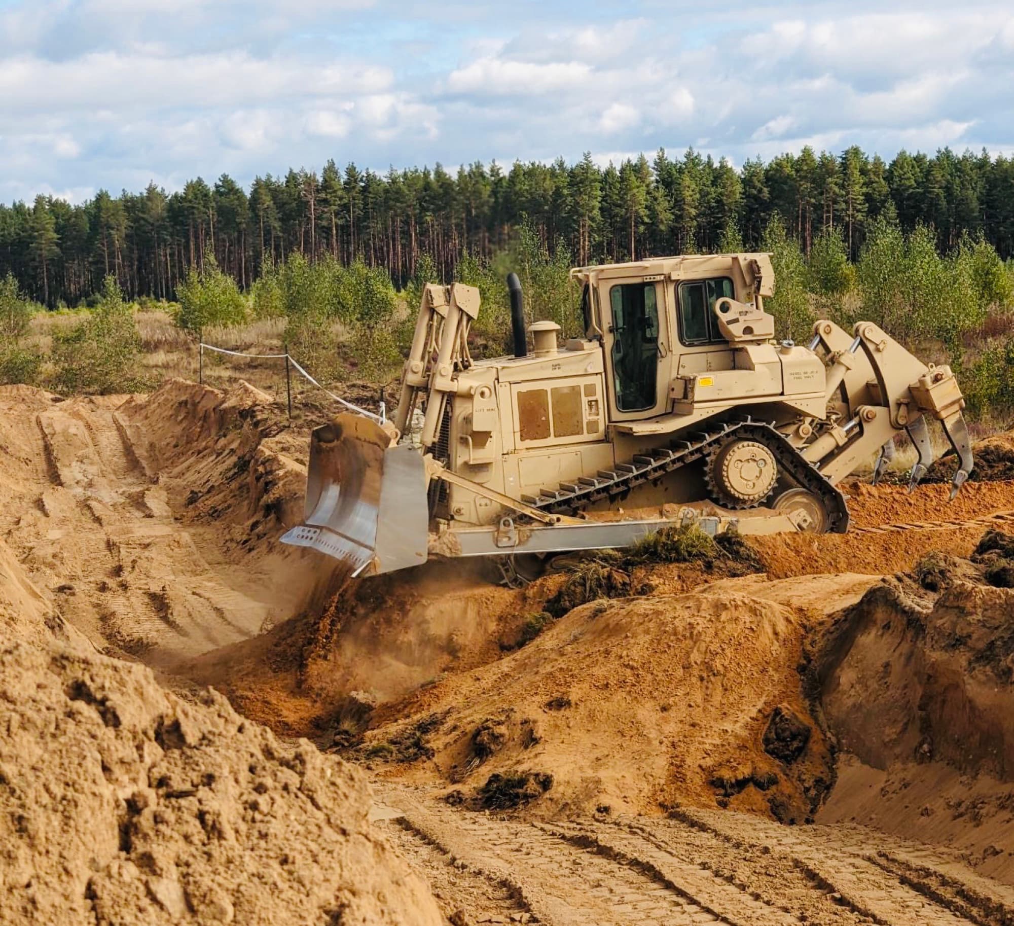 A U.S. Army armored combat engineer bulldozer cutting a breach through earthworks at a training range