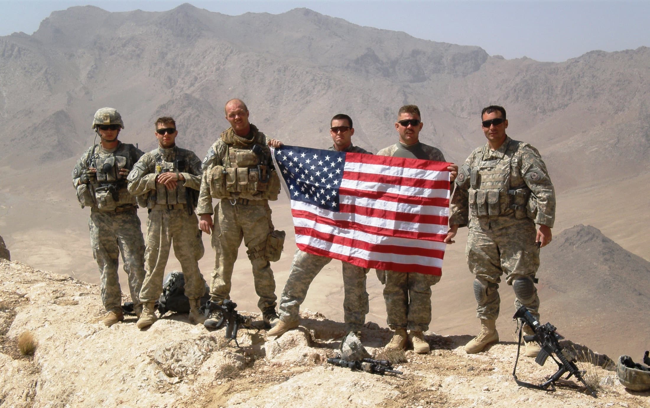 Six U.S. soldiers stand on an Afghan mountain ridge holding the American flag between them