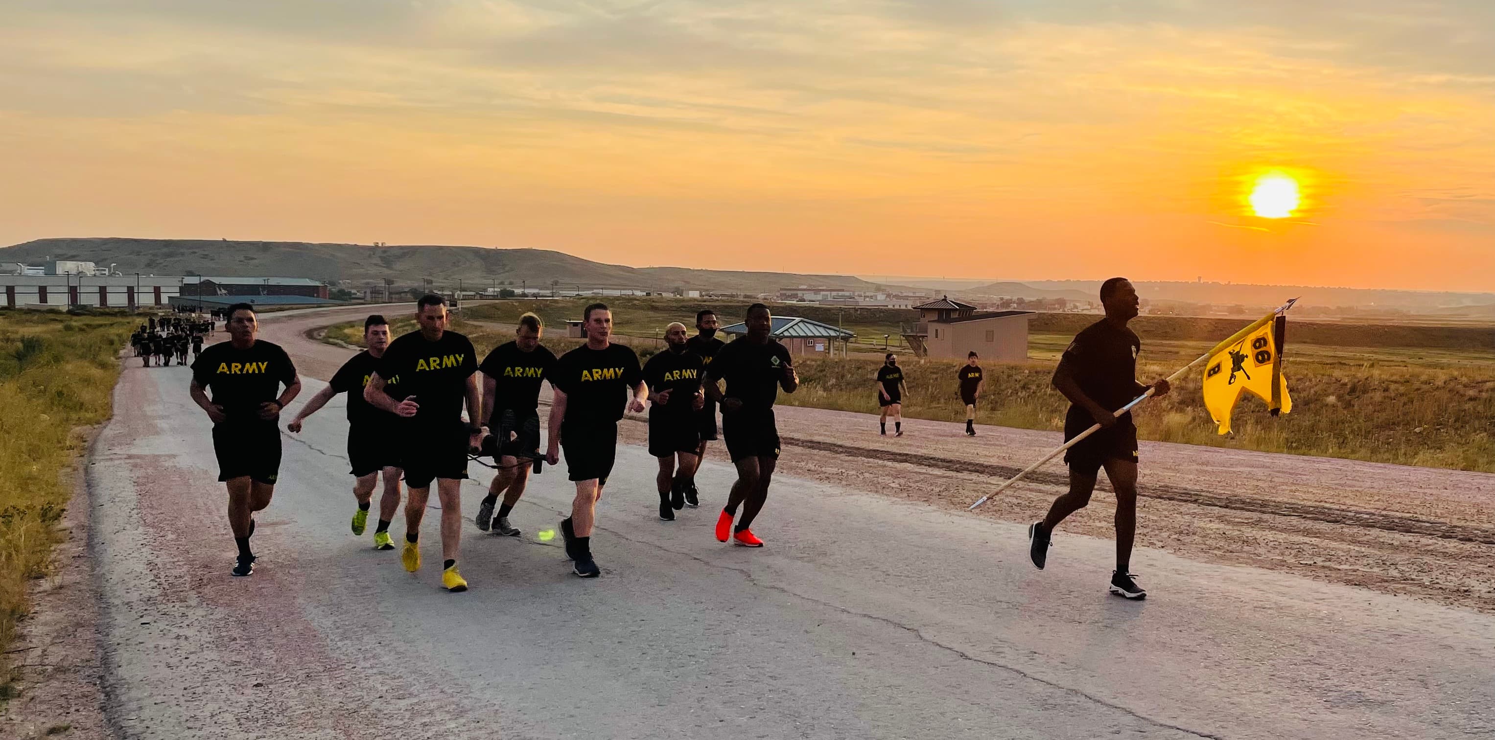 U.S. Army soldiers in PT gear running at sunrise with a unit guidon — the kind of shared formation Roll Call keeps connected after the uniform comes off