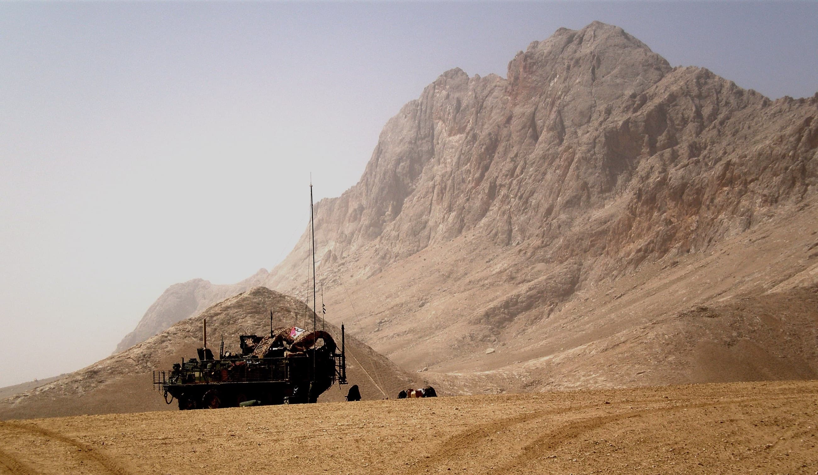 A U.S. Army Stryker on patrol across open desert beneath a towering Afghan ridgeline